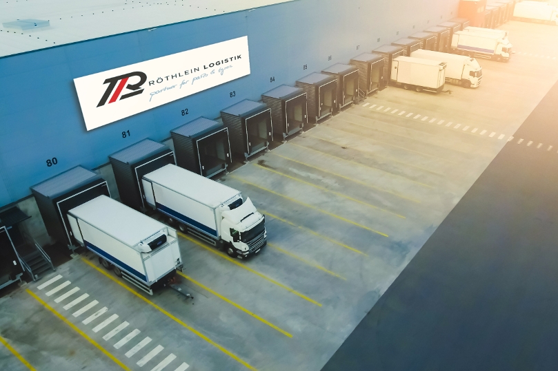 Logistikhalle von außen/oben mit mehreren Lkw vor Laderampen